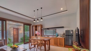 Eine moderne Küche mit Holzschränken, eine Essecke mit Tisch und Stühlen sowie ein großes Fenster mit Jalousien.