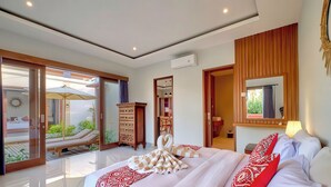 Ein geräumiges Schlafzimmer mit einem großen Bett, einem Holzschrank, einem Spiegel und einer Glastür, die auf einen Balkon mit Liegestuhl führt.