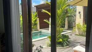 Eine moderne Villa mit einer Holzterrasse, einem Pool und üppiger tropischer Bepflanzung.