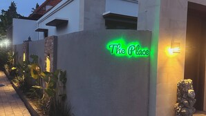 Ein Gebäude mit einer Neonreklame mit der Aufschrift 'The Place' und einer Steinstatue am Eingang.