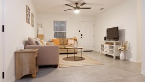 A living room with a sofa, coffee table, and TV stand. - Charming Crestview Stay 4 Bedrooms, Prime Location (Crestview)