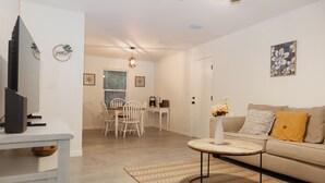 A modern living room with a sofa, coffee table, and TV stand. There is a dining area with chairs and a table in the background. - Charming Crestview Stay 4 Bedrooms, Prime Location (Crestview)