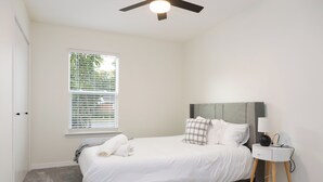 A bedroom with a bed, a bedside table with a lamp, a window with blinds, and a ceiling fan. - Charming Crestview Stay 4 Bedrooms, Prime Location (Crestview)