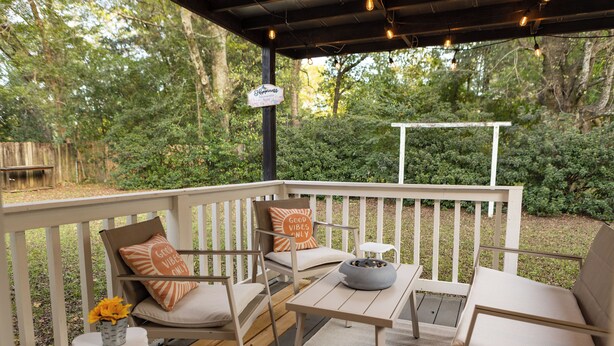 A covered outdoor seating area with white railings, cushioned chairs, a table, and a sign indicating a 'Happy Hour' event. - Charming Crestview Stay 4 Bedrooms, Prime Location (Crestview)