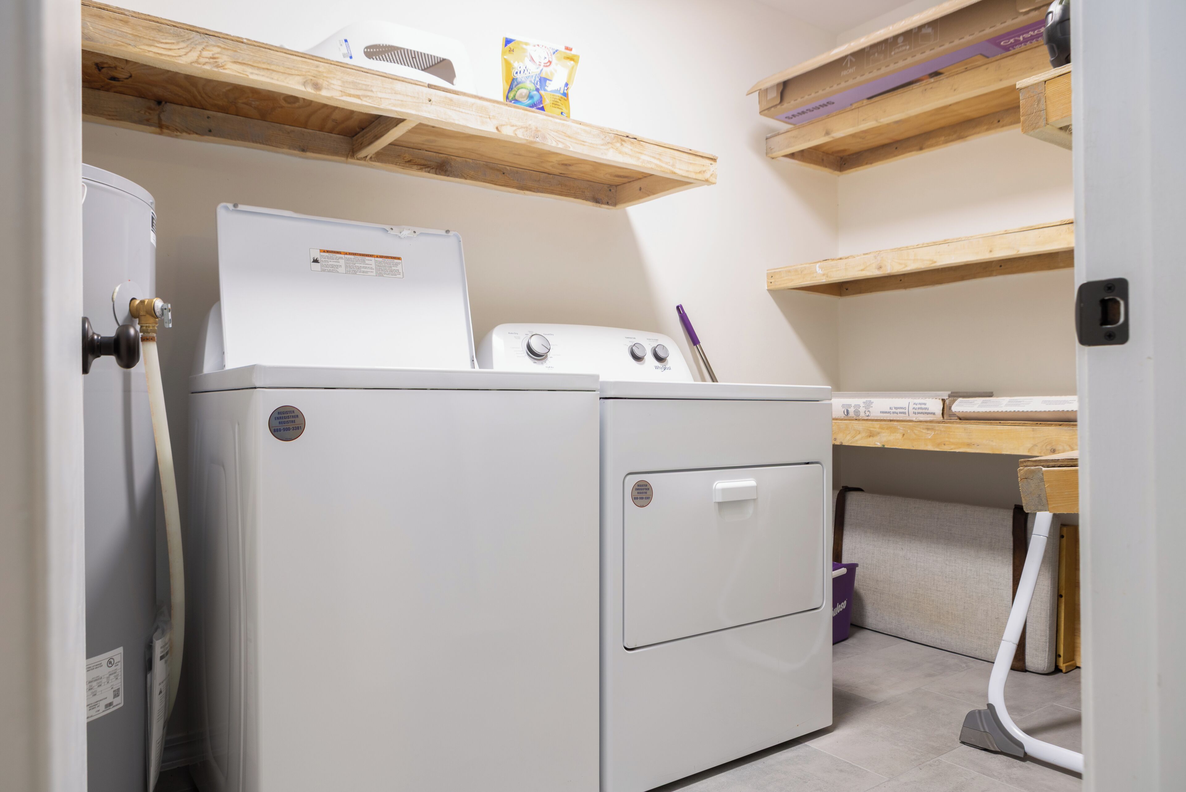A laundry area with a washing machine and dryer, wooden shelves above, and a vacuum cleaner.