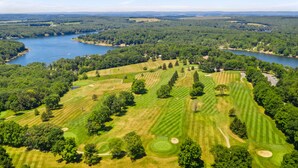 An aerial view of a golf course with multiple fairways and greens, surrounded by dense forests and a large body of water. - Indian Lake, Lucky 7 Chalet (Central City)