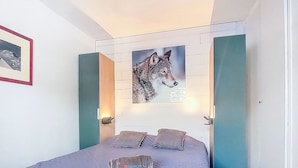 A bedroom with a bed, a wall-mounted painting of a wolf, and a door with a light switch.