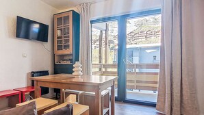 A room with a wooden table and chairs, a TV mounted on the wall, and a sliding glass door leading to an outdoor area.