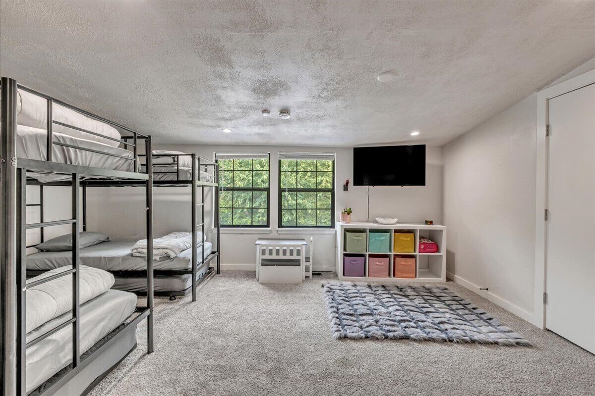 Une chambre avec des lits superposés, un radiateur blanc, un téléviseur fixé au mur et un meuble de rangement avec des bacs de différentes couleurs.