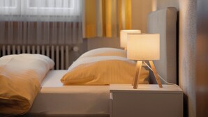 A neatly made bed with a white and yellow duvet, a bedside table with a lamp, and a window with curtains. - BeKb-Gebäude Apt 07 by Interhome (Wengen)