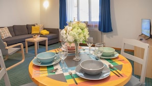 A dining area with a round table set for four, surrounded by chairs. There is a sofa and a small table with a yellow cushion in the background. - BeKb-Gebäude Apt 07 by Interhome (Wengen)