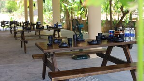 A covered outdoor dining area with wooden tables and benches, surrounded by greenery. - Baya Beach Club (Xuan Loc)