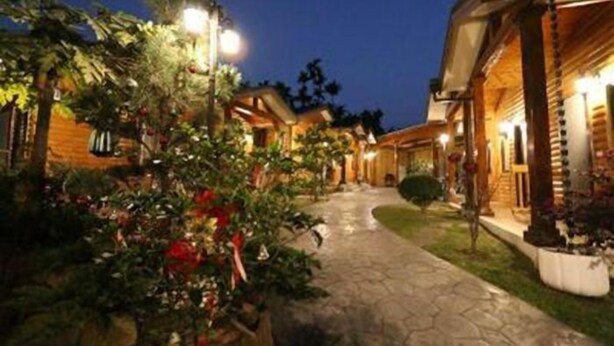 Un sendero conduce a una hilera de cabañas de madera con iluminación exterior y abundante vegetación.
