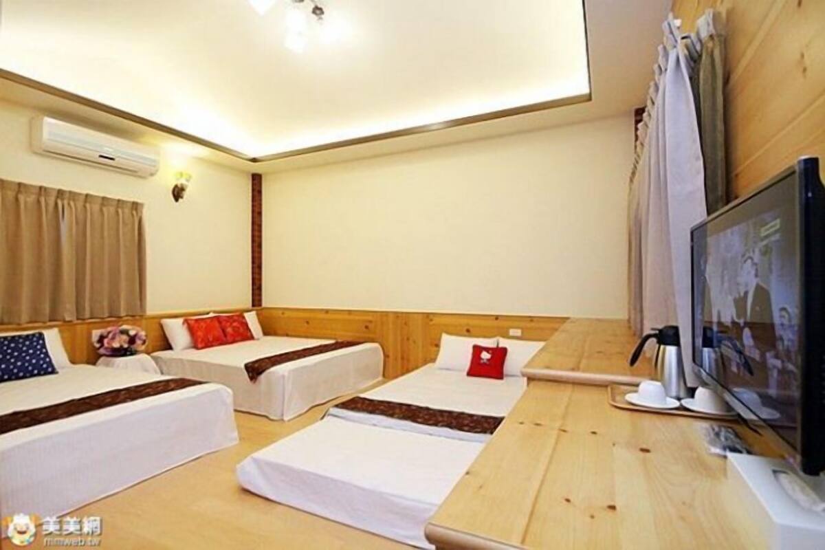Habitación de hotel con dos camas individuales, un escritorio de madera, un televisor y un equipo de aire acondicionado.