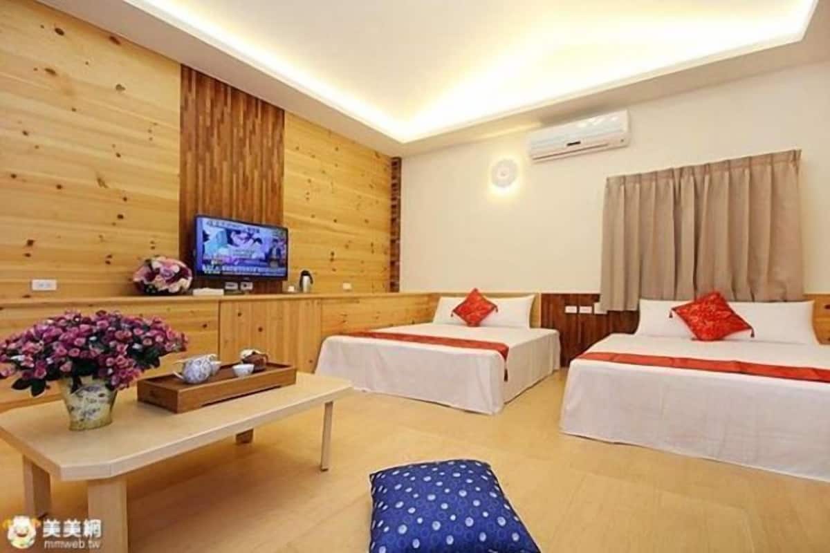 Habitación de hotel con dos camas, televisión, pared de madera y una mesita con un jarr ón de flores.