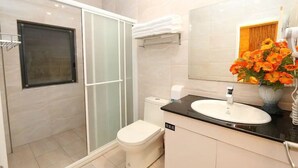 Un baño moderno con cabina de ducha de vidrio, inodoro blanco, lavabo con encimera negra y espejo con arreglo floral.