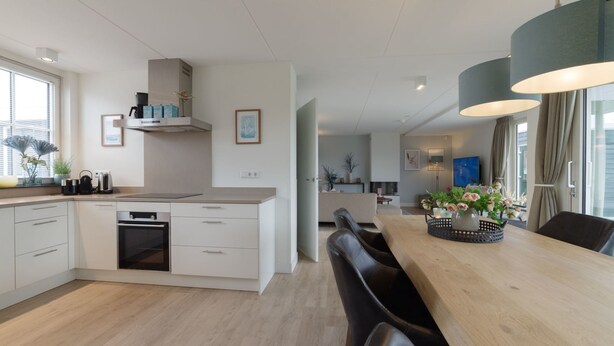 Una cocina moderna con armarios blancos, horno empotrado y comedor con mesa y sillas de madera.