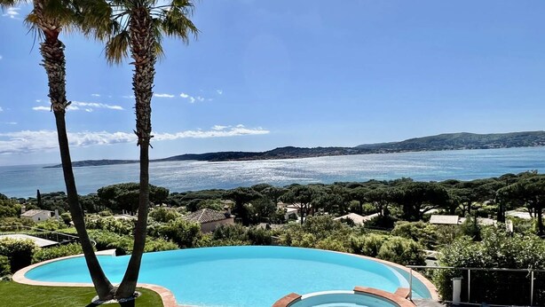 Una piscina con vista sul mare, circondata dal verde e da una zona patio con sedie.