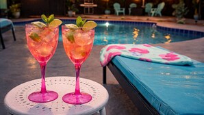 Duas taças com uma bebida rosa e folhas de hortelã sobre uma mesa redonda à beira da piscina.