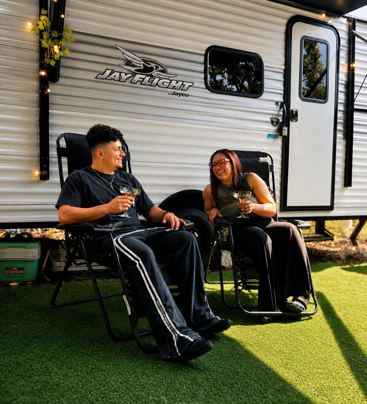 Deux personnes assises sur des chaises à l’extérieur d’un camping-car Jayco, tenant des boissons.