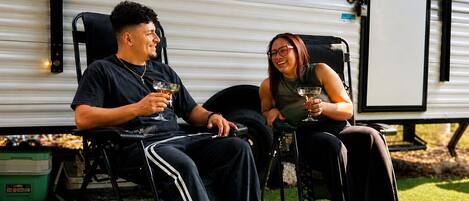 Deux personnes assises sur des chaises à l’extérieur d’un camping-car Jayco, tenant des boissons.
