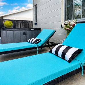 Two outdoor lounge chairs with striped cushions, a small flower arrangement, and a building with a white exterior and window blinds. - Experience the charm of East Winter Park with a cozy glamping RV. (Winter Park)