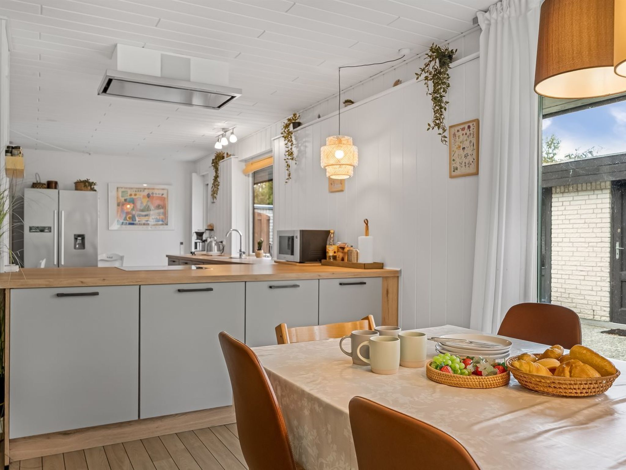 Une cuisine moderne avec des meubles blancs, un plan de travail en bois et un coin repas avec une table dressée pour deux personnes.