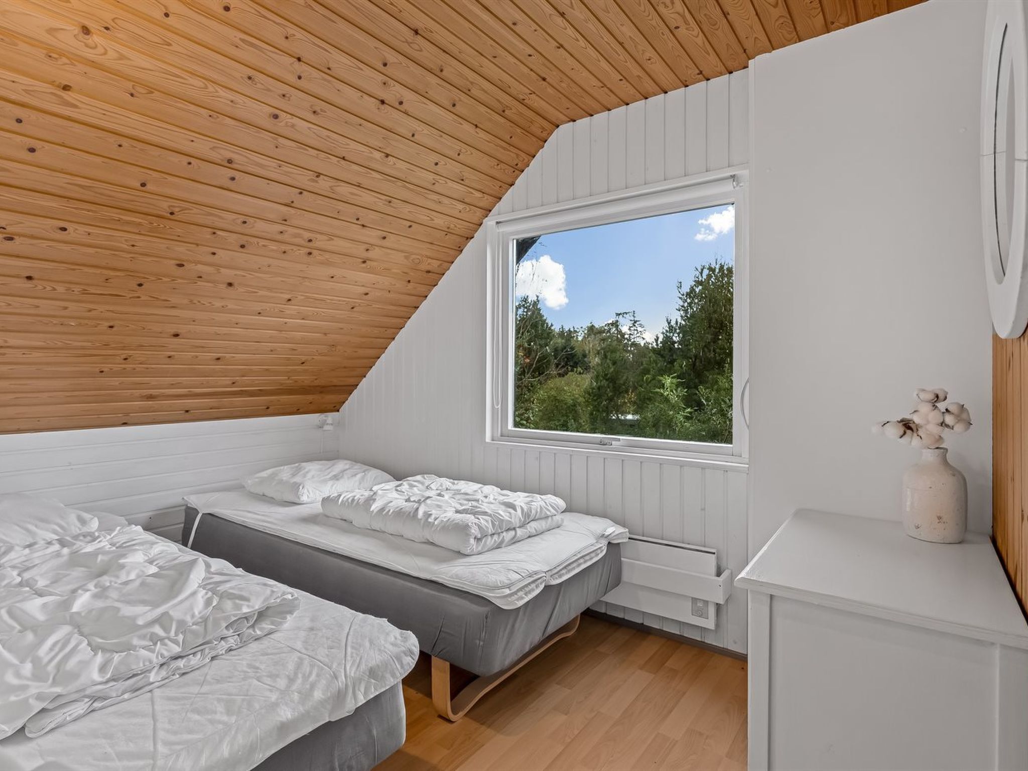 Une chambre avec un plafond en pente, deux lits, une fenêtre et un radiateur.