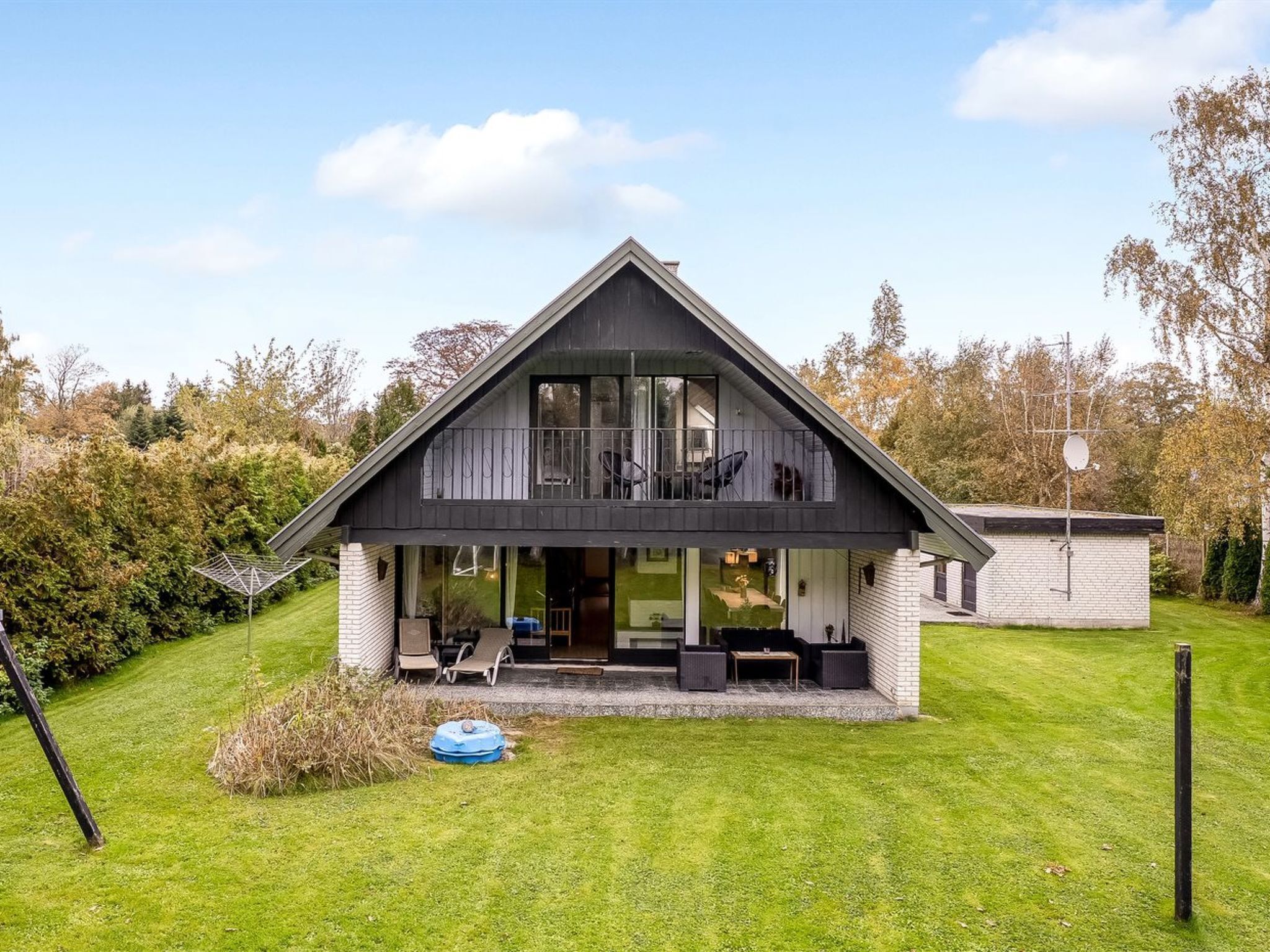 A modern two-story house with a large balcony, a covered patio, and a well-maintained lawn.