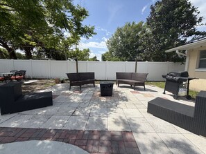 An outdoor patio with a grill, seating, and a white fence. - Anysel Pool house (Orlando)
