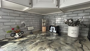 Una cucina con piano di lavoro in marmo, zoccolo posteriore in mattoni grigi e mobili bianchi.