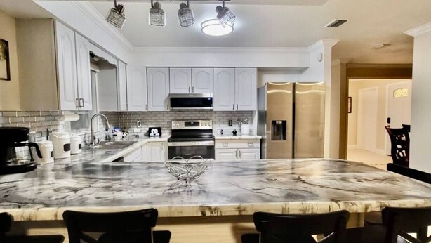 Una cucina moderna con mobili bianchi, un'isola in marmo e un frigorifero in acciaio inossidabile.