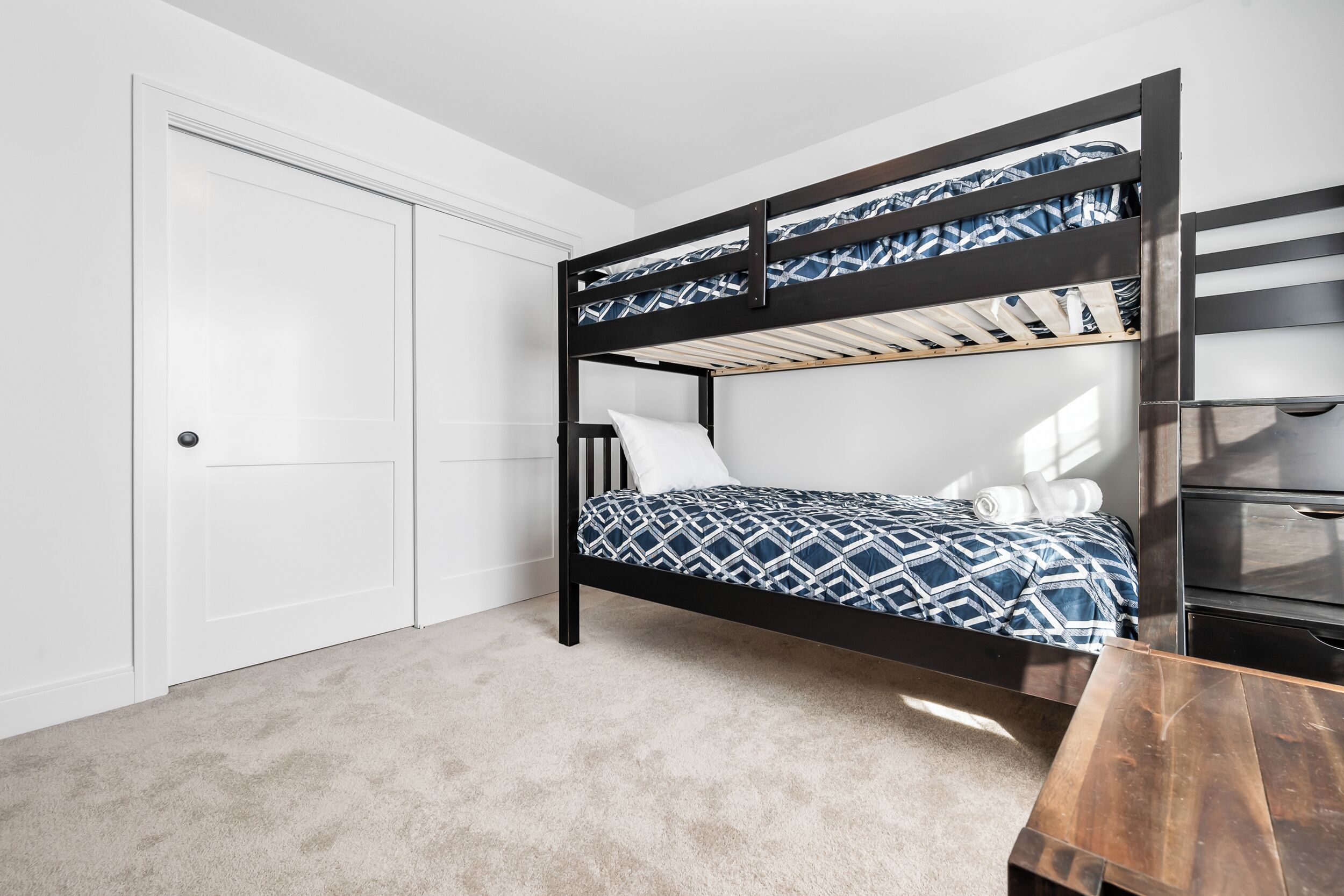 A bunk bed with a geometric patterned bedspread, a white door, and a wooden bench.