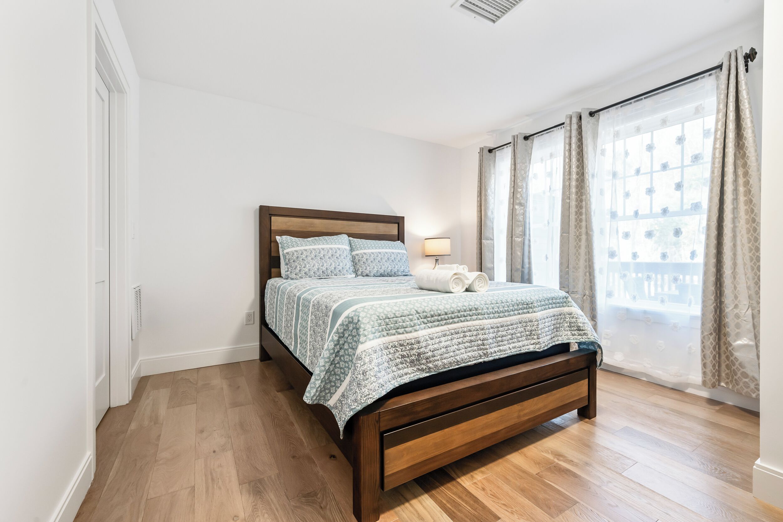 A bedroom with a wooden bed, a bedside lamp, and a window with curtains.