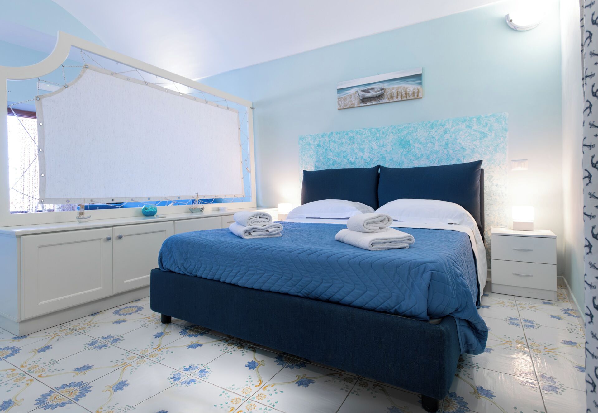 A bedroom with a bed, a nightstand, a mirror, and a window with a view.