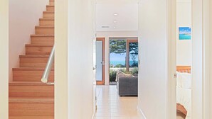 A hallway with a wooden staircase, a view of the outdoors, and a bed in the adjacent room.
