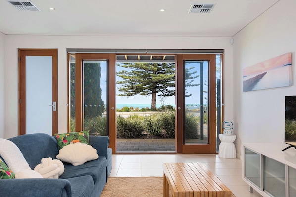 A modern living room with a sofa, a coffee table, and a view through glass doors to a beach.