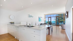 A modern kitchen with white cabinetry, a large island, and a view of the outdoors through large windows.