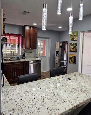 A kitchen with granite countertops, stainless steel appliances, and pendant lighting.