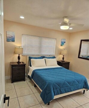 A bedroom with a bed, two nightstands, a ceiling fan, and wall art.