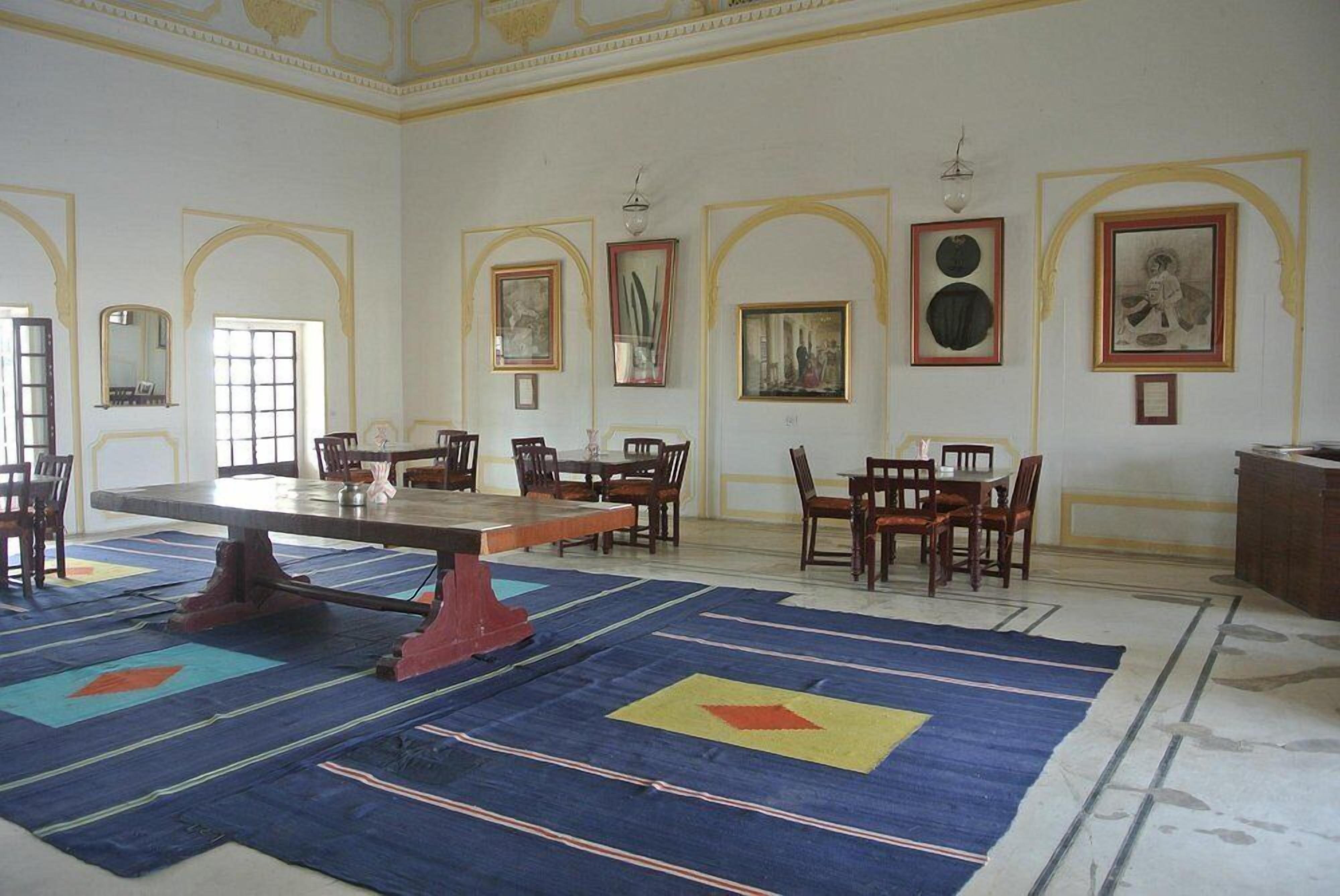 Una habitación amplia con una gran mesa y varias sillas, obras de arte enmarcadas en las paredes y una alfombra estampada.