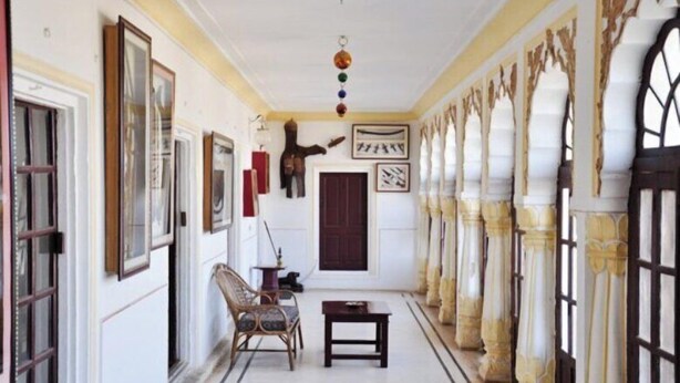 A hallway with a patterned floor, framed pictures on the walls, a wooden chair, and a table. - Roopangarh Fort  (Roopangarh)