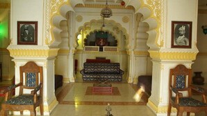 A traditional interior with ornate arches, a central sofa, and two wooden chairs. - Roopangarh Fort  (Roopangarh)