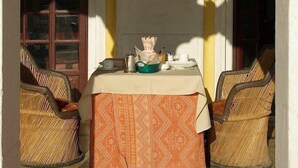 A room with a table set for two, two wicker chairs, a framed picture on the wall, and a door with a window. - Roopangarh Fort  (Roopangarh)