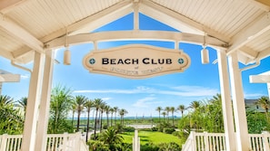 Schild eines Beachclubs mit Palmen und Blick auf das Meer.