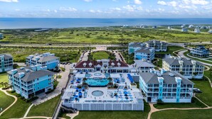 Un complex turístic amb diversos edificis, una zona de piscina central i vista a l'oceà.
