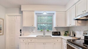 A kitchen with white cabinetry, a built-in oven, a stovetop, and a window with blinds. - The Jefferson 222 - St Pete (St. Petersburg)