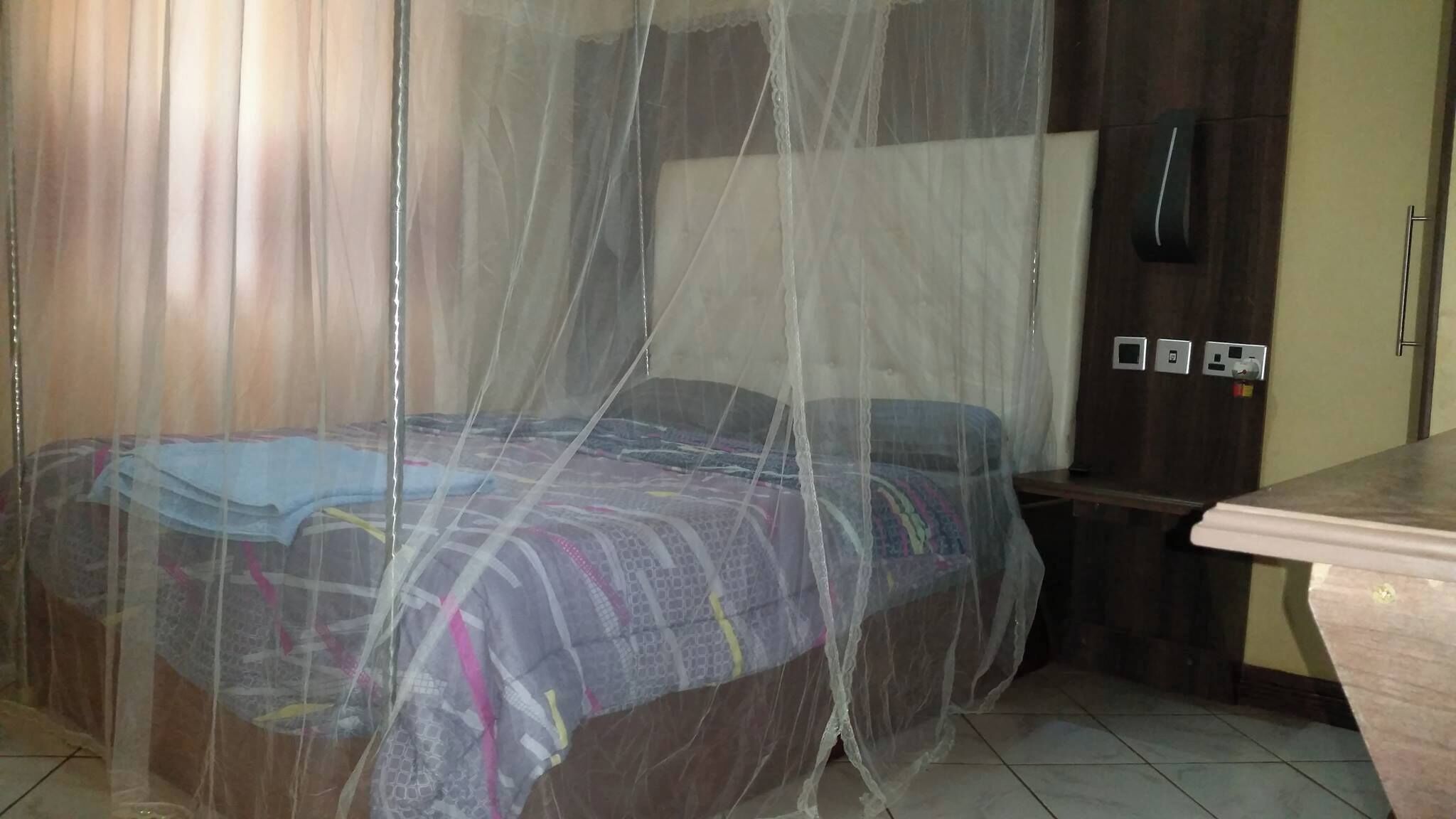A bedroom with a bed covered by a mosquito net, a wooden headboard, and a nightstand with a lamp.