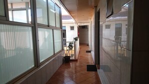 A corridor with large windows, a tiled floor, and a potted plant.