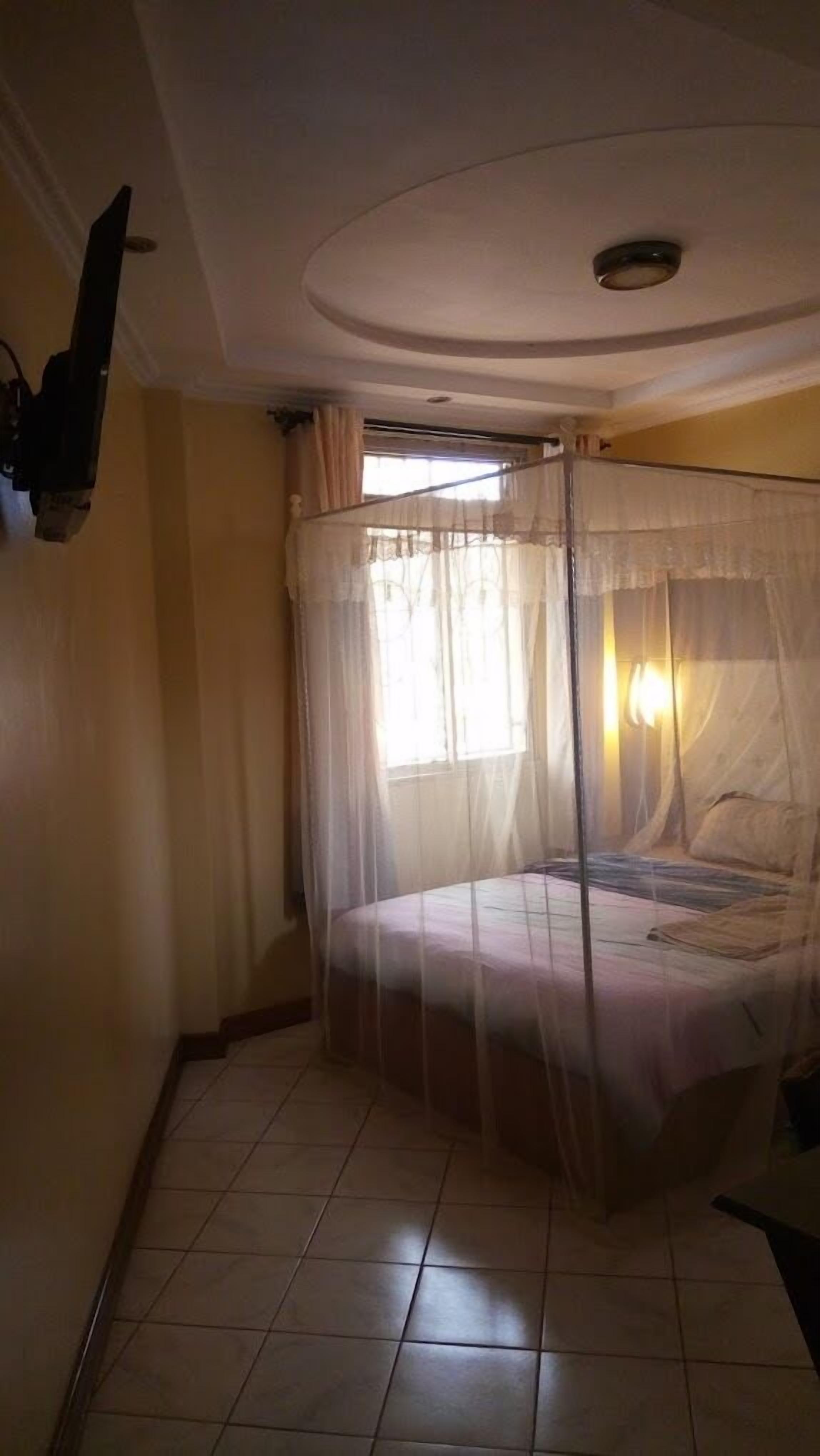 Une chambre à coucher avec un lit recouvert d’une moustiquaire, une fenêtre avec des rideaux et un luminaire au plafond.